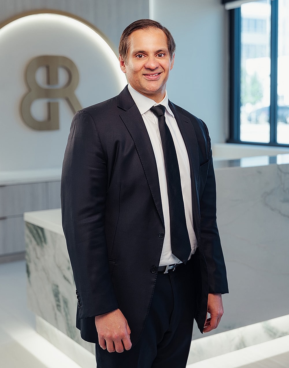 Houston tummy tuck surgeon, Dr. Ravi, in formal attire standing indoors.