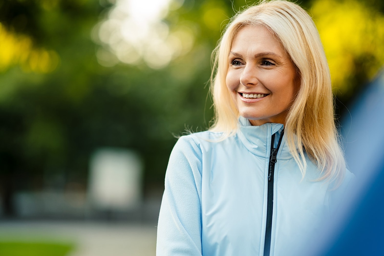 Smiling woman in light blue jacket outdoors.