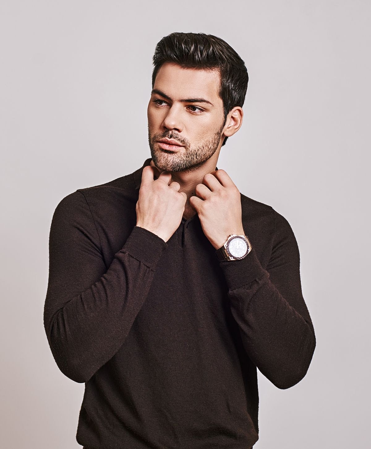 Man adjusting collar with wristwatch, studio portrait.