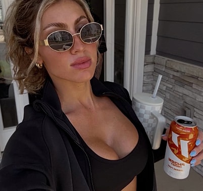 Person in sunglasses holding a beverage outdoors.