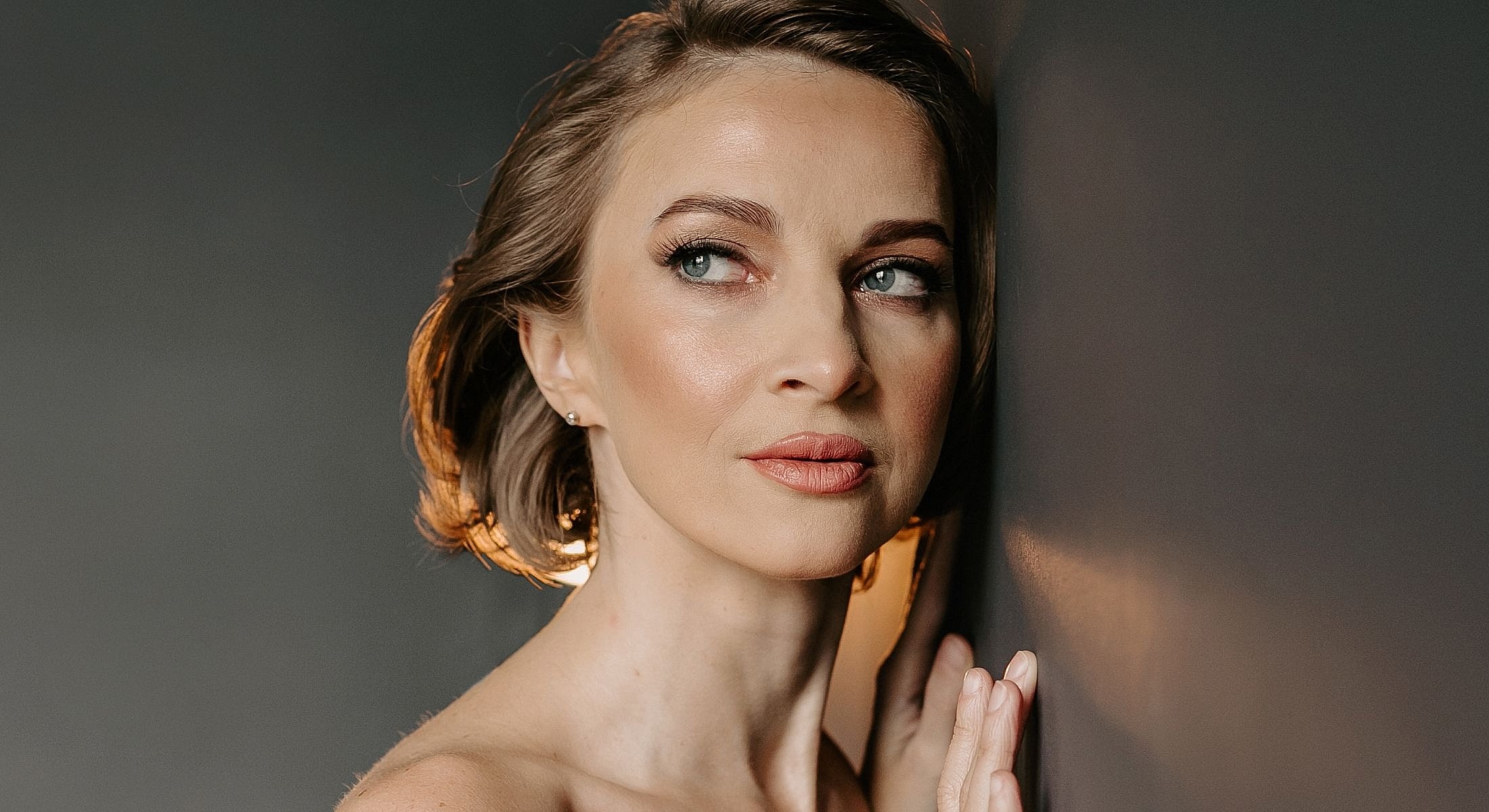 Woman gently touching wall, looking thoughtfully off-camera.
